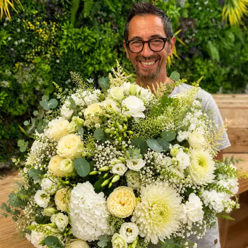 Le fleuriste d'Au Delà des Fleurs, tout sourire, avec un bouquet blanc dans sa boutique de Gujan-Mestras