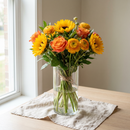 Bouquet Éclat Solaire, tournesols, roses orange et renoncules jaunes dans un vase en verre